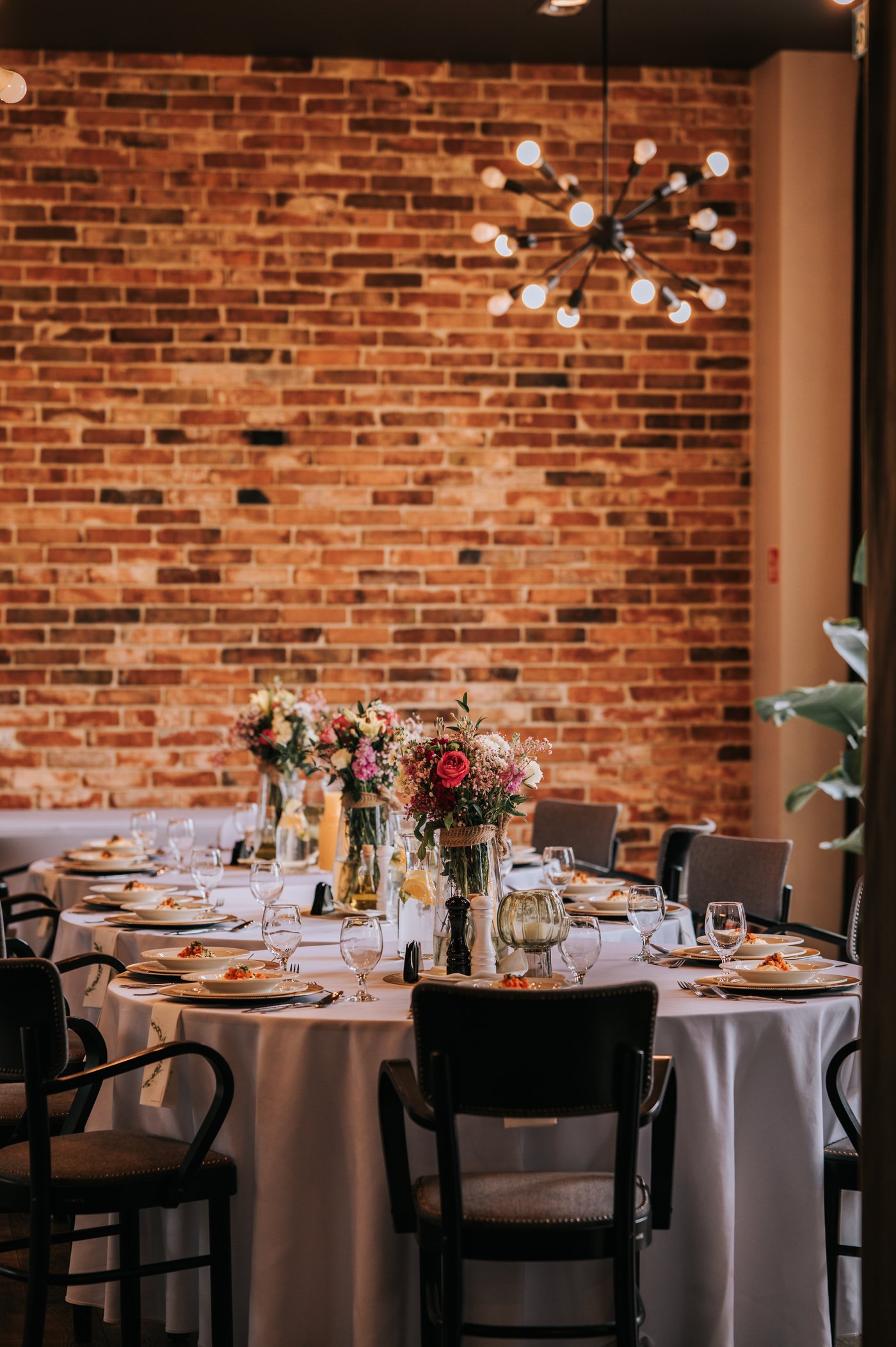 Sztolnia interior — brick wall, sputnik chandelier, round table with pink rose bouquets