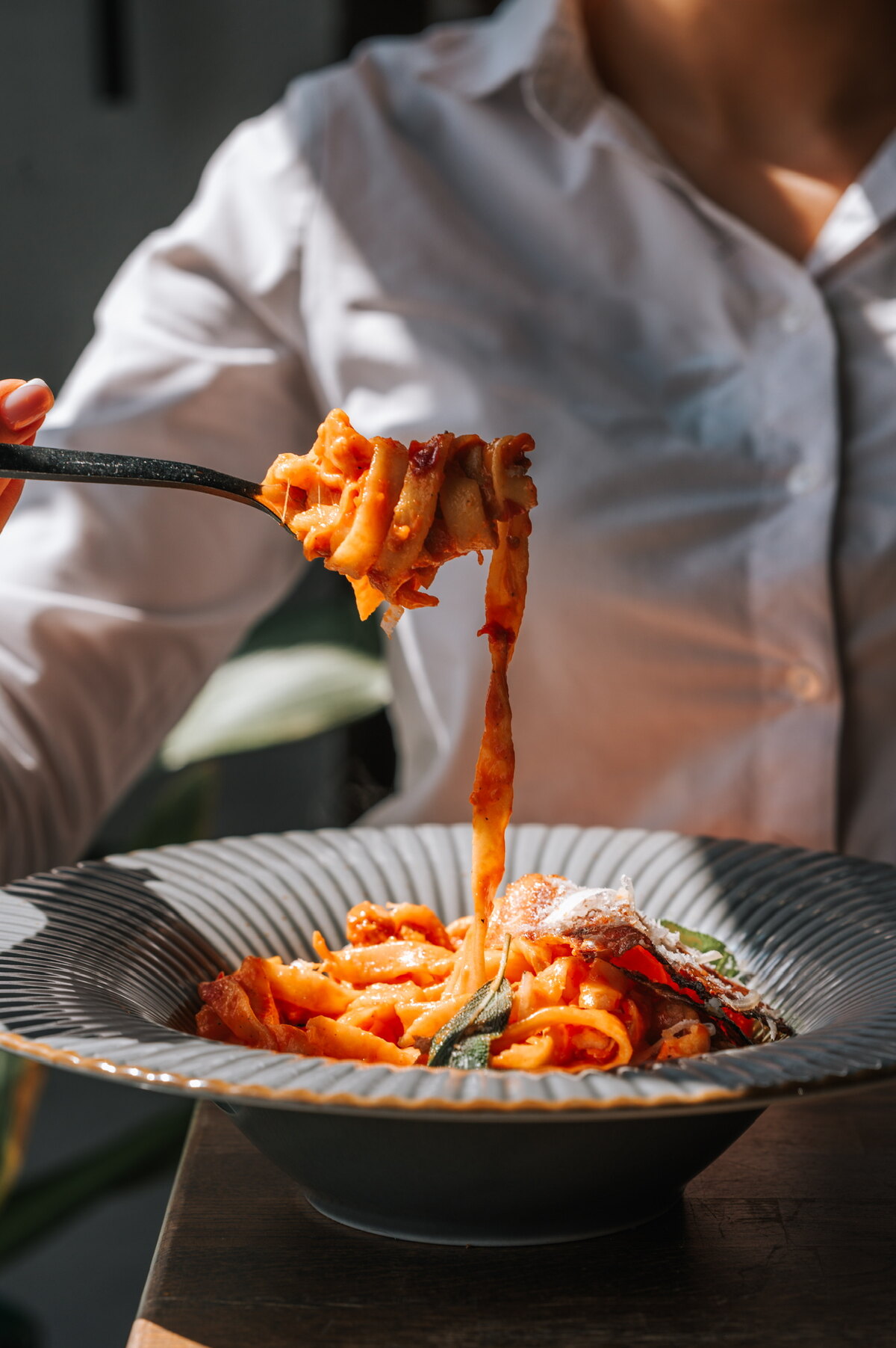 Hands twirling pappardelle in tomato sauce with parmesan — guest at the table